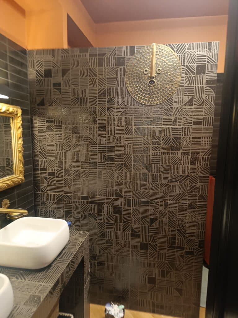 Carrelage mural géométrique noir et vasque moderne chic Vasque blanche sur comptoir assorti devant un mur de carrelage noir géométrique avec une grande horloge dorée.