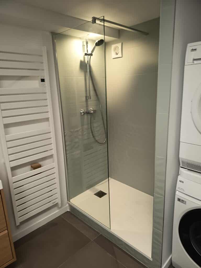 Douche à l'italienne moderne et aménagement de salle de bain Douche à l'italienne moderne avec paroi en verre, sèche-serviette blanc et lave-linge AEG empilé.