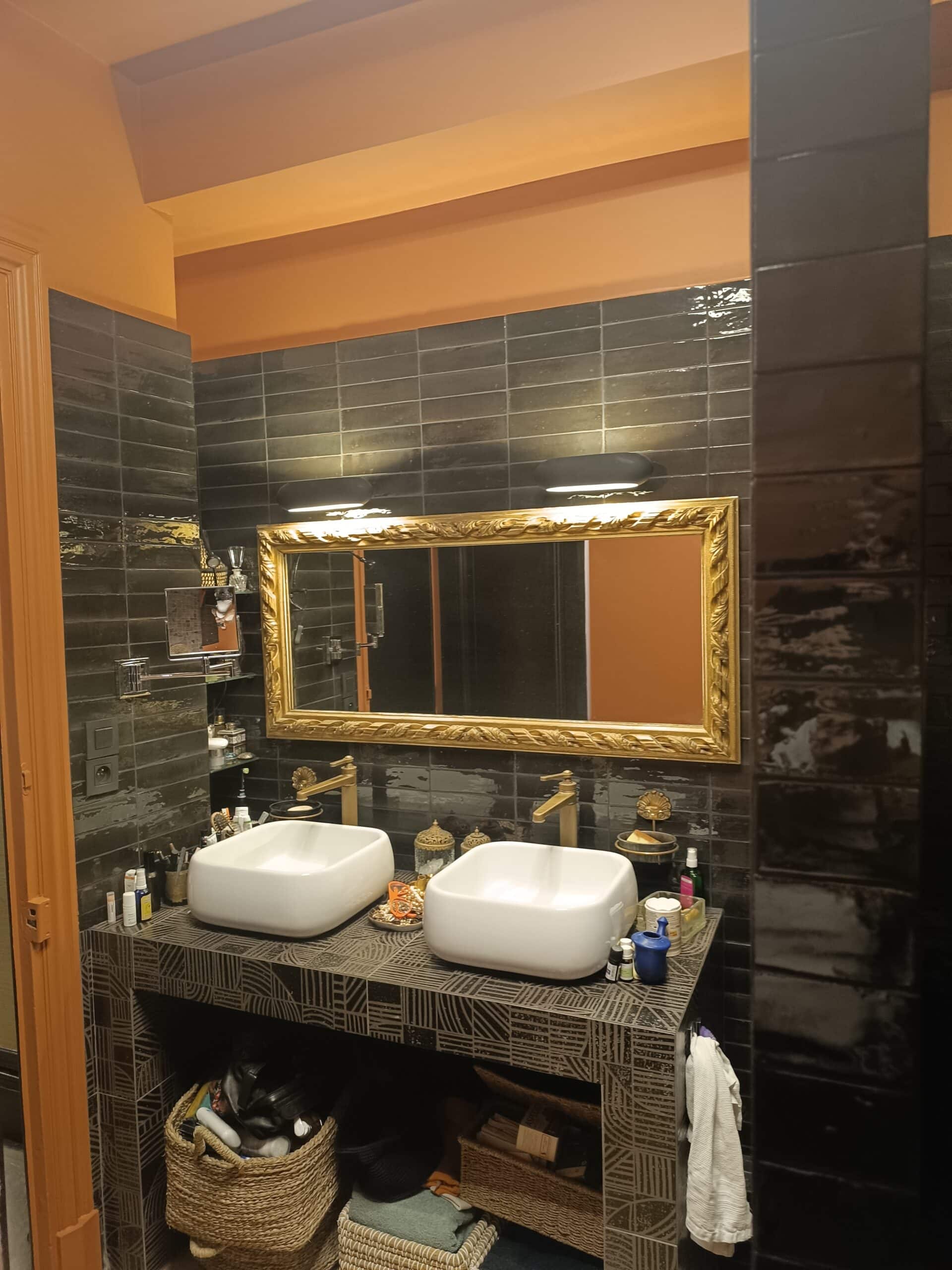Salle de Bain Chic avec Double Vasque et Miroir Doré Double vasque design, robinets dorés et grand miroir à cadre sculpté devant un mur en carrelage noir texturé.